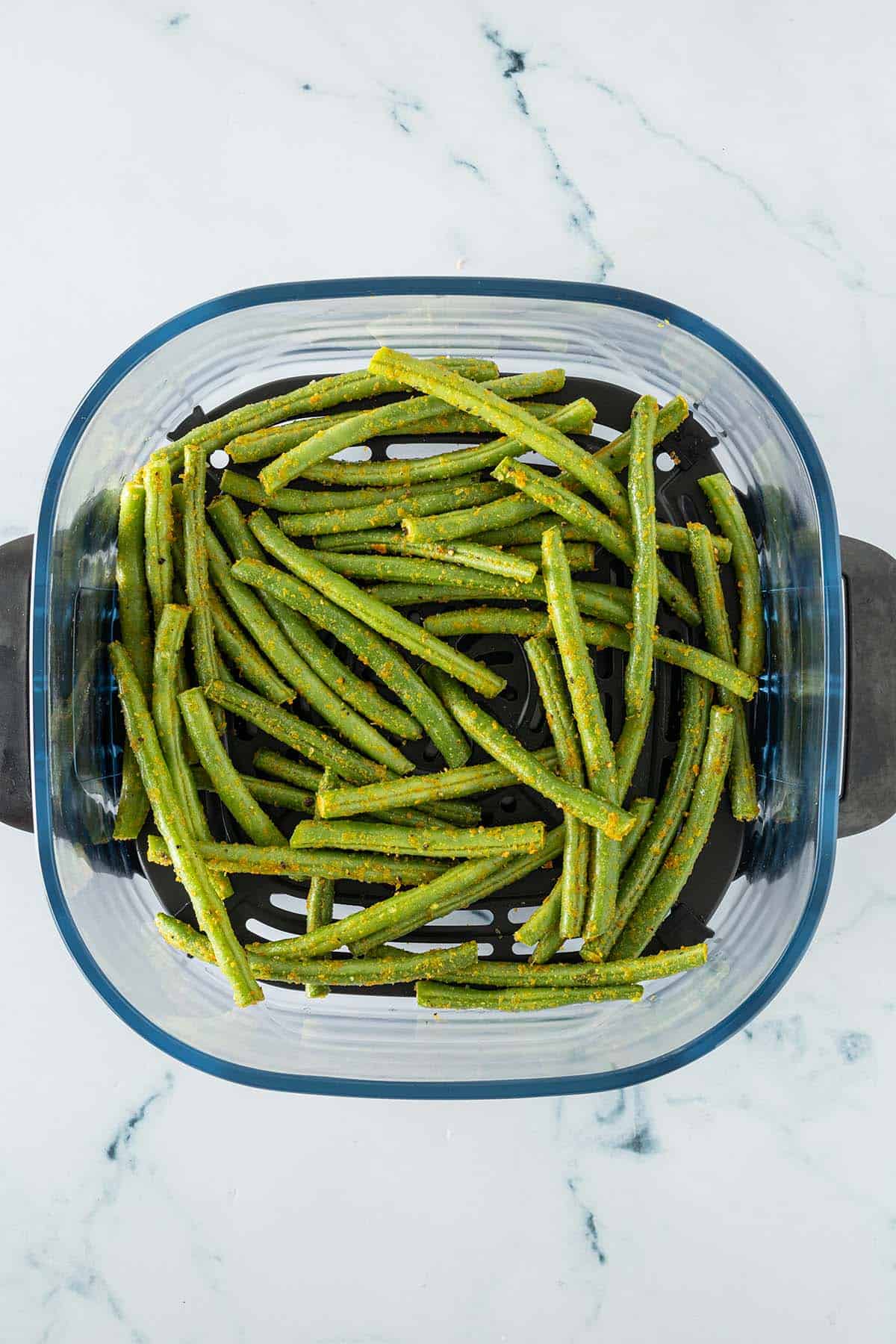Mit Hefeflocken marinierte gr&uuml;ne Bohnen in einem Airfryer-Korb.