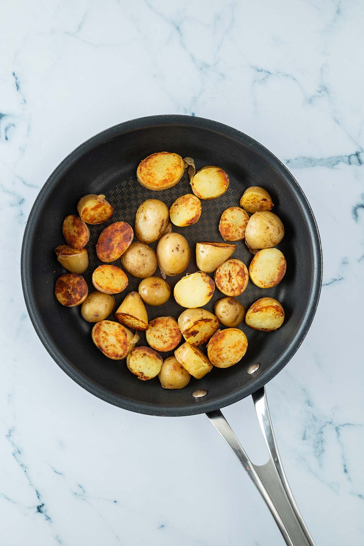 Knusprig angebratene Kartoffelh&auml;lften in einer Pfanne.