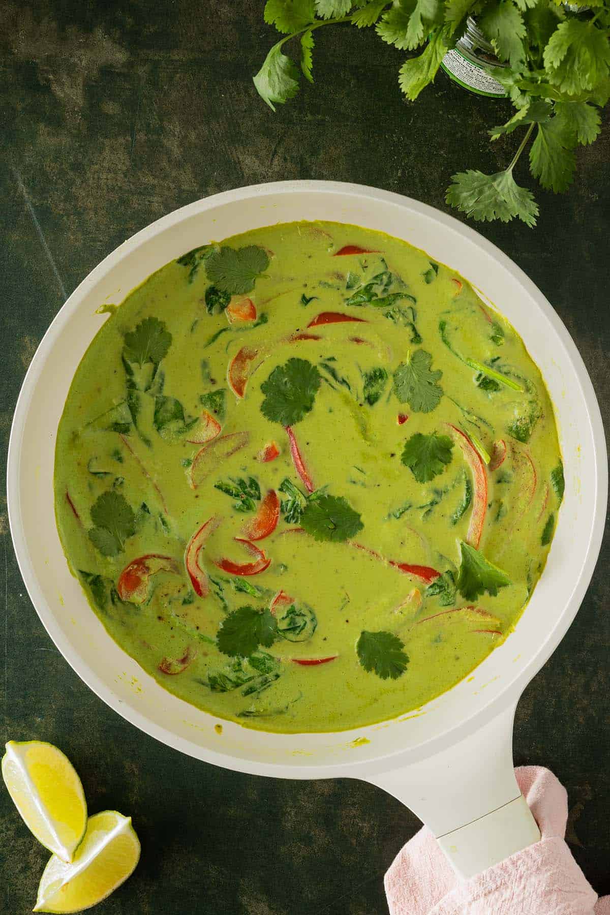 Cremiges gr&uuml;nes Thai Curry in einer Pfanne mit Gem&uuml;se, serviert auf einem dunkelgr&uuml;nen Untergrund.