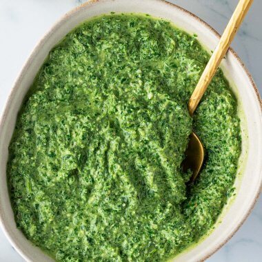Sch&uuml;ssel mit einer Gr&uuml;nkohl Pesto auf einem Marmor-Untergrund, mit einer Flasche &Ouml;l und einer Sch&uuml;ssel Pinienkerne im Bildrand.