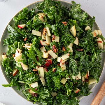 Frischer Gr&uuml;nkohlsalat auf einem gro&szlig;en Teller mit Apfel und N&uuml;ssen, Deko im Bildrand.