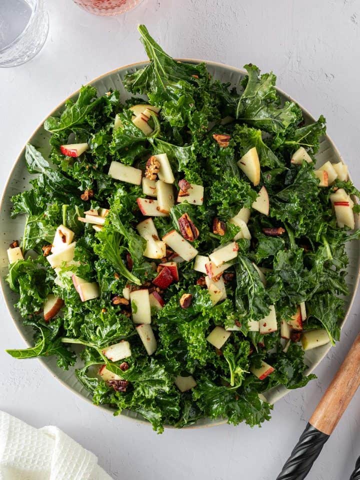 Frischer Gr&uuml;nkohlsalat auf einem gro&szlig;en Teller mit Apfel und N&uuml;ssen, Deko im Bildrand.
