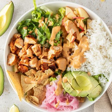 H&auml;hnchen Bowl mit Reis, Salat, Avocado, Zwiebeln, Nackos und cremigen Dressing, Deko im Bildrand.