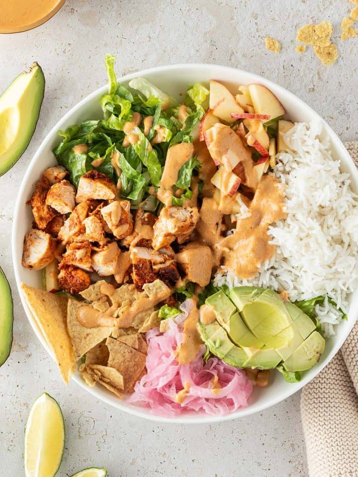 H&auml;hnchen Bowl mit Reis, Salat, Avocado, Zwiebeln, Nackos und cremigen Dressing, Deko im Bildrand.