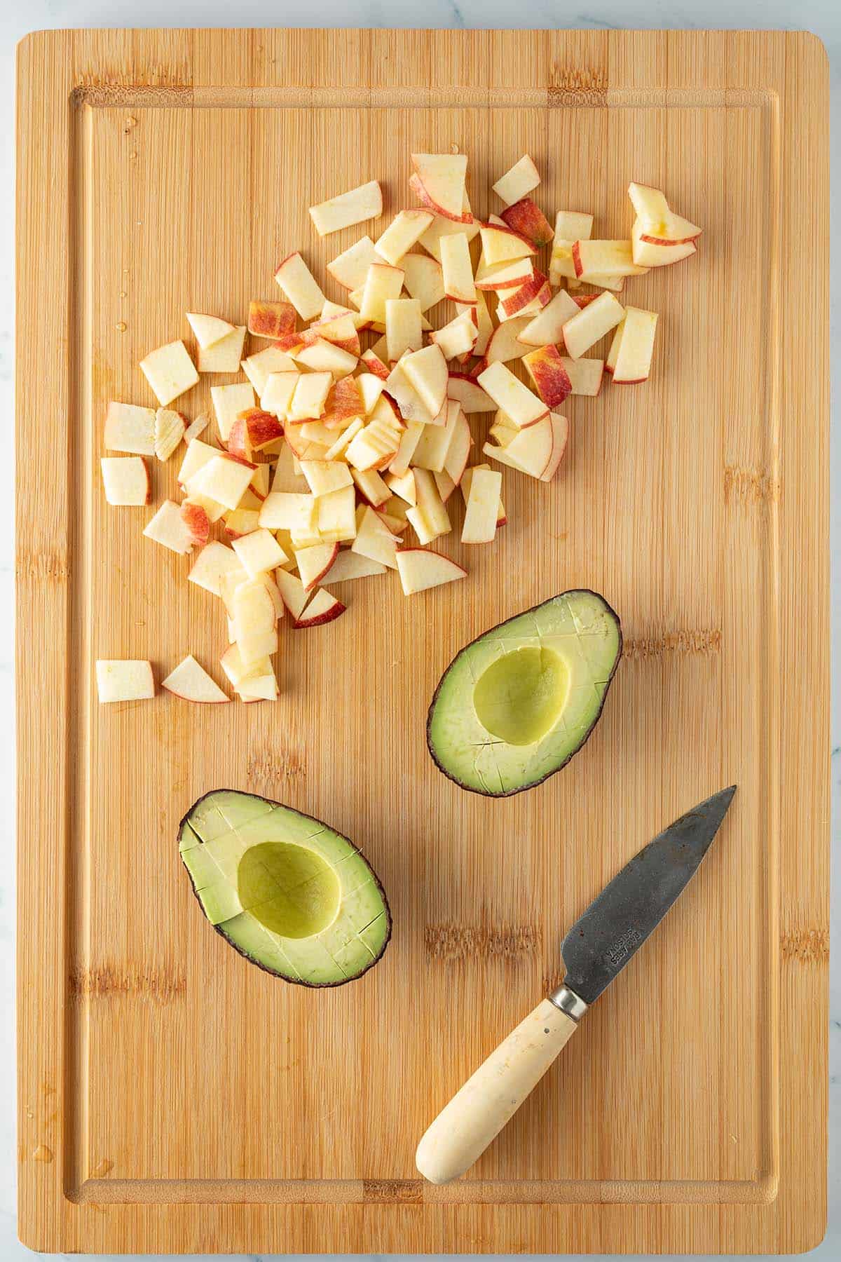 Halbierte Avocado und d&uuml;nne Apfelscheiben auf einen Brett mit Messer.