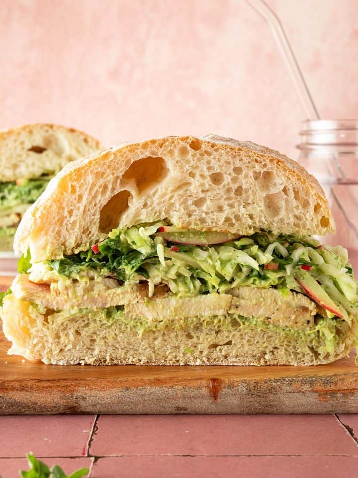 Aufgeschnittenes Ciabatta-Sandwich mit peruanischem H&auml;hnchen, Wei&szlig;kohl-Apfelsalat und cremiger gr&uuml;ner Sauce auf einem Holzbrett.
