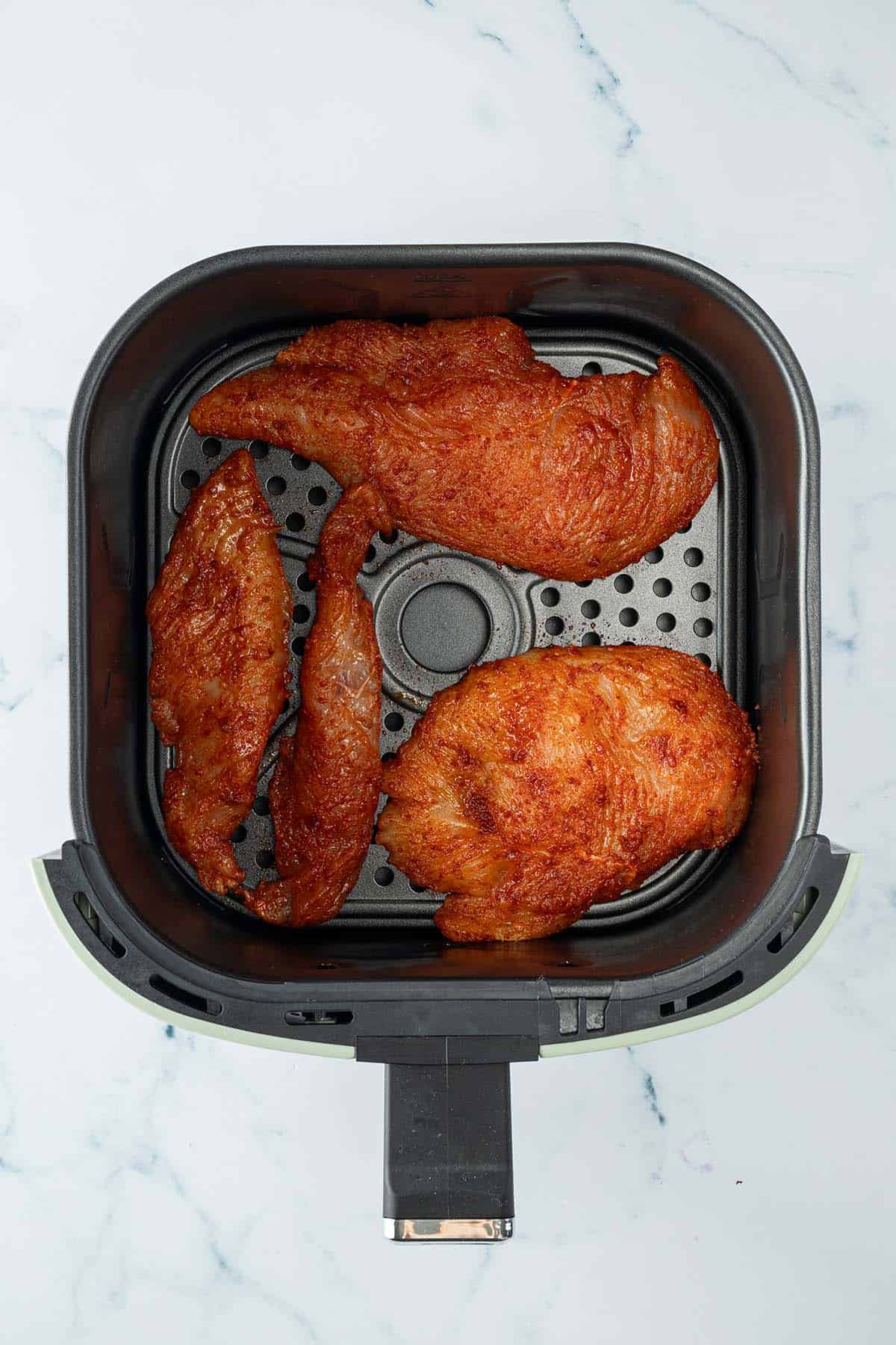 D&uuml;nne, marinierte H&auml;hnchenfilets in einem Airfryer-Korb.