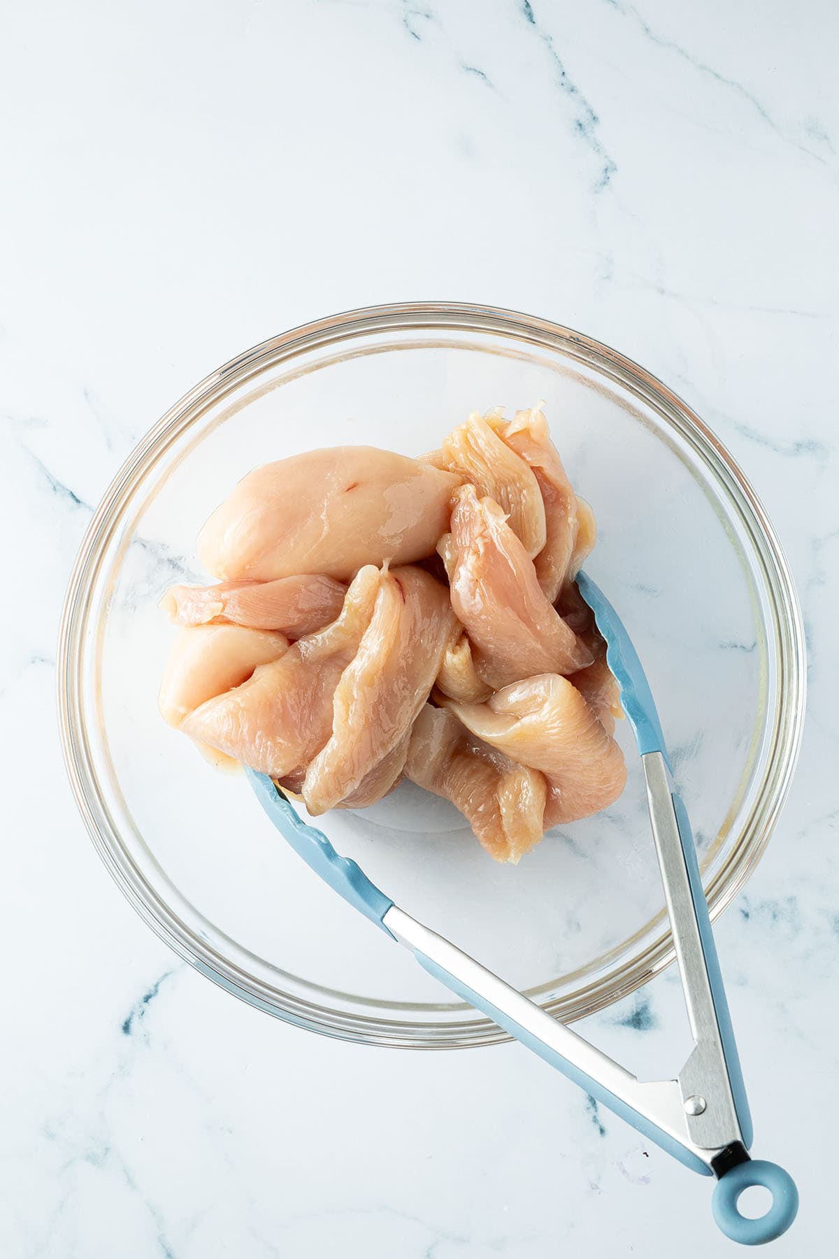 Kleine, d&uuml;nne H&auml;hnchenfilets werden in einer Sch&uuml;ssel mit &Ouml;l verrmischt.