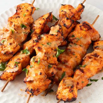 Mehrere Chicken Satay H&auml;hnchenspie&szlig;e auf einem Teller, serviert mit einer Erdnusssauce und frischen Kr&auml;utern.