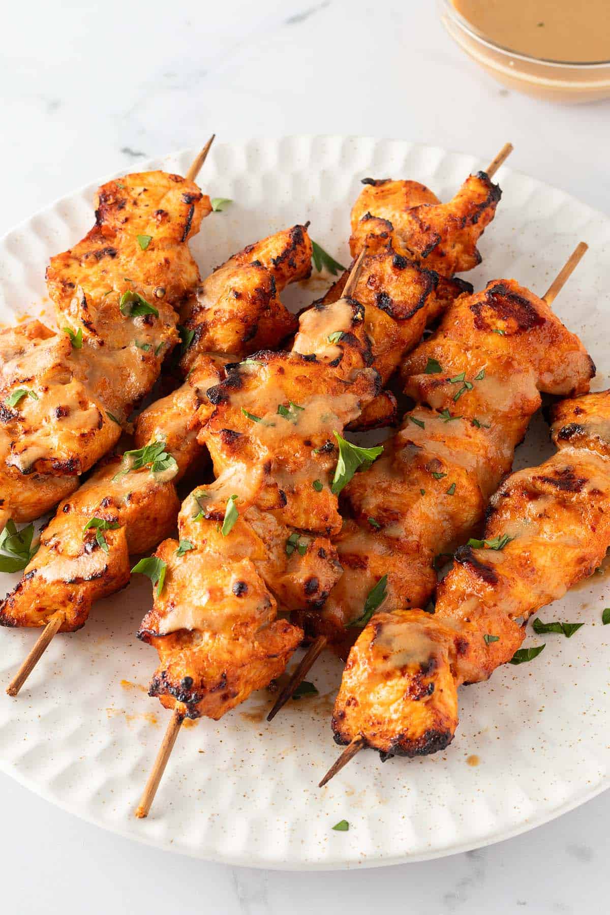 Mehrere Chicken Satay H&auml;hnchenspie&szlig;e auf einem Teller, serviert mit einer Erdnusssauce und frischen Kr&auml;utern.