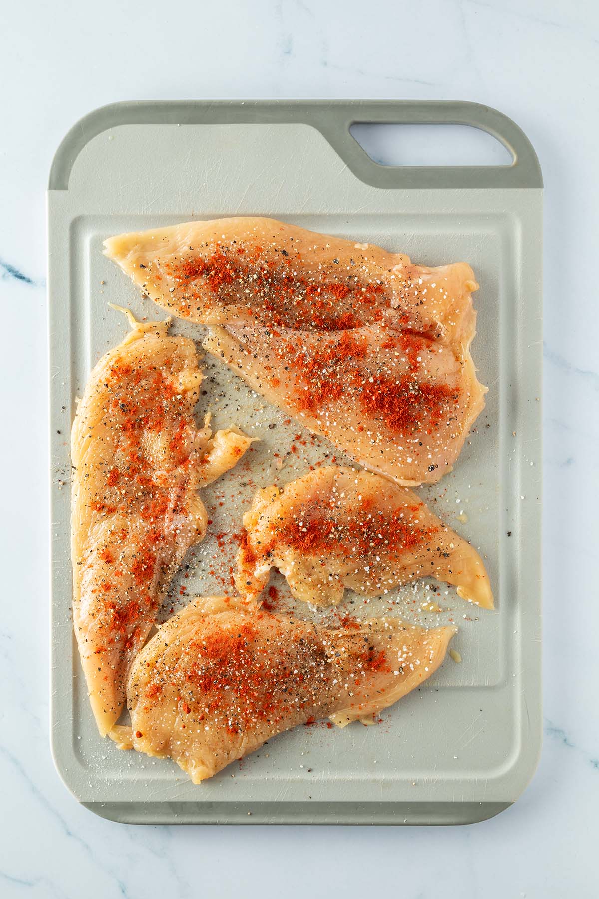 D&uuml;nn geklopfte und gew&uuml;rzte H&auml;hnchenbrustfilets auf einem Brett.