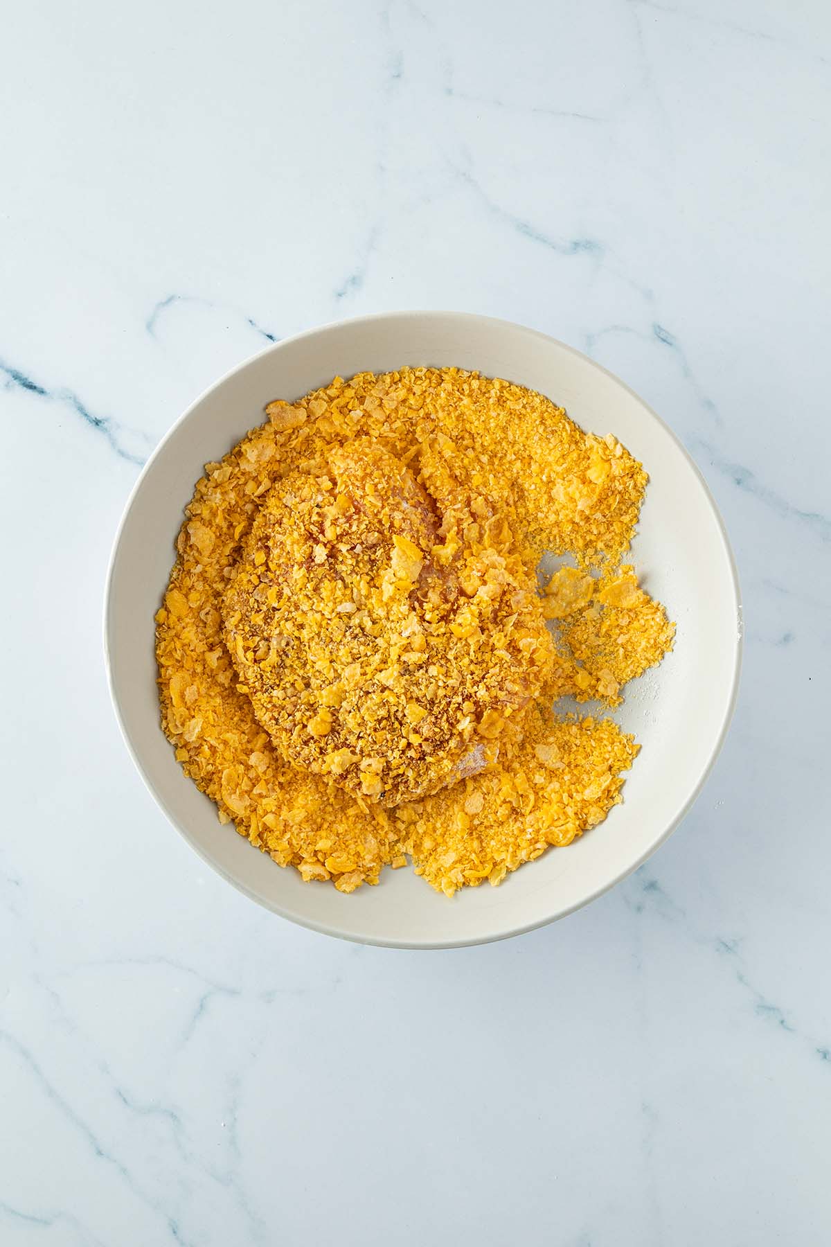 H&auml;hnchenfleisch wird in einer Sch&uuml;ssel mit zerkleinerten Cornflakes paniert.