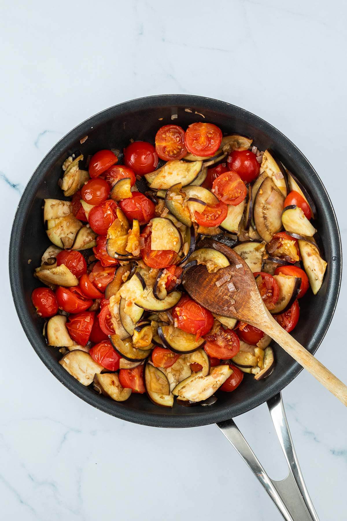 Angebratene Auberginenscheiben und halbierte Kirschtomaten in einer Pfanne.