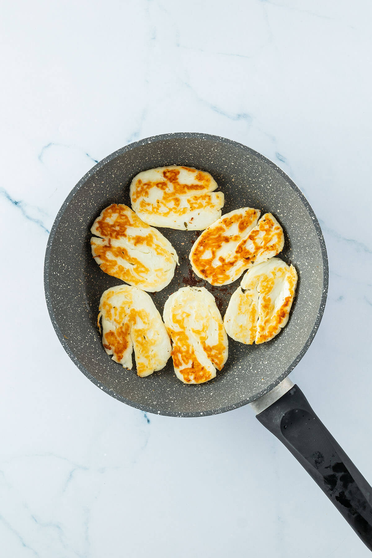 Knusprig gebratene Halloumi-Scheiben in einer Pfanne.