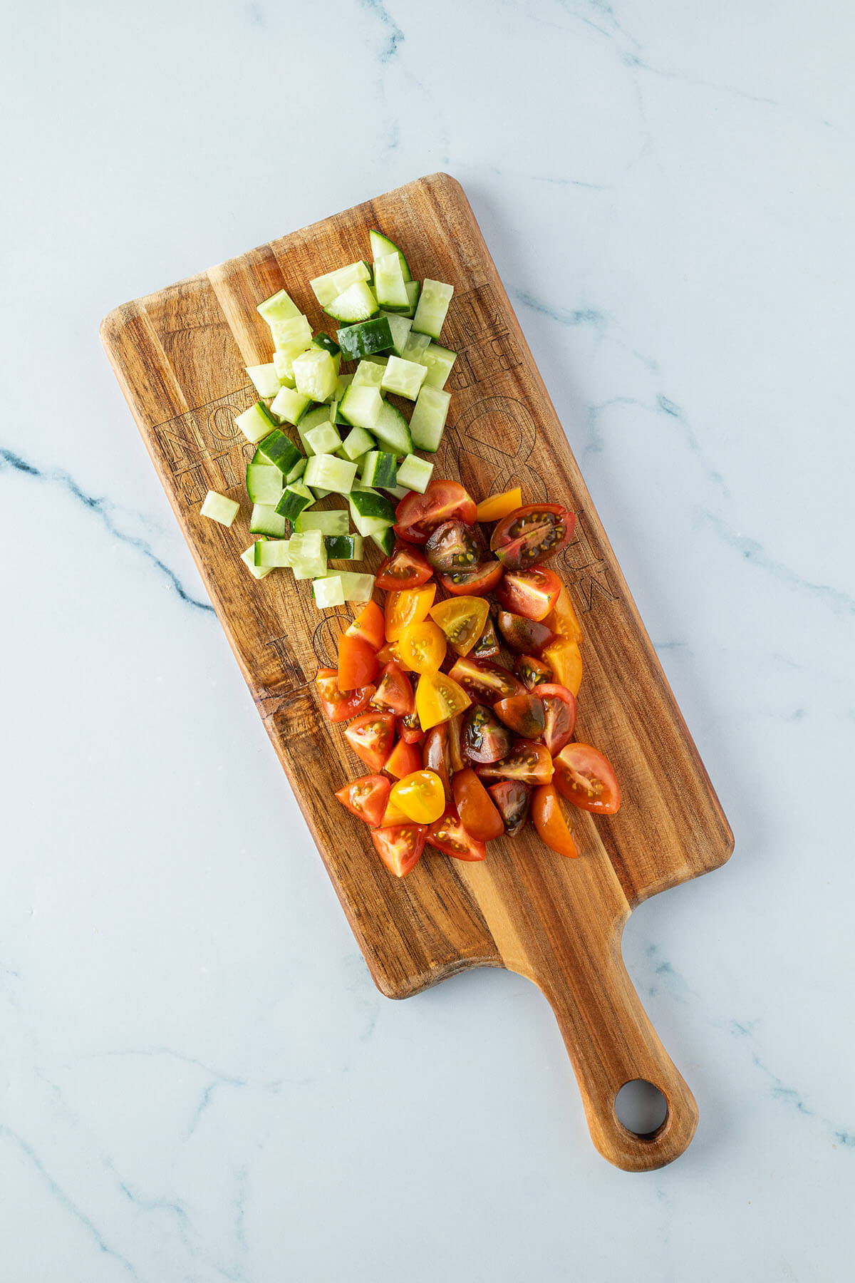 Kleingeschnittene Tomaten und Gurkenst&uuml;cke auf einem Holzbrett.
