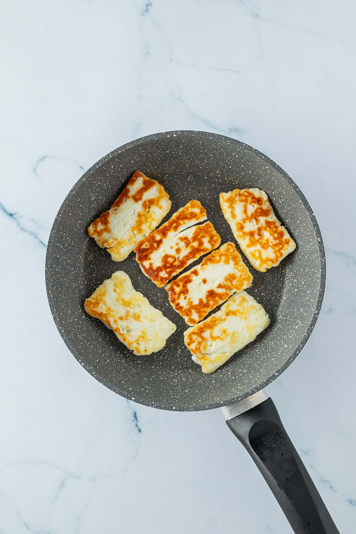 Goldbraun gebratene Halloumi-Scheiben in einer Pfanne.