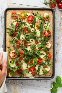 Ofenpfannkuchen auf einem Blech belegt mit Tomaten, Mozzarella und Rucola.
