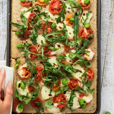 Ofenpfannkuchen auf einem Blech belegt mit Tomaten, Mozzarella und Rucola.