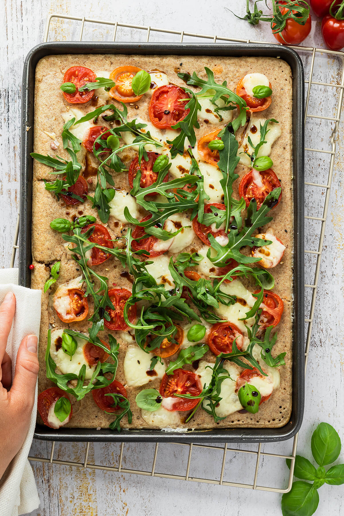 Ofenpfannkuchen auf einem Blech belegt mit Tomaten, Mozzarella und Rucola.