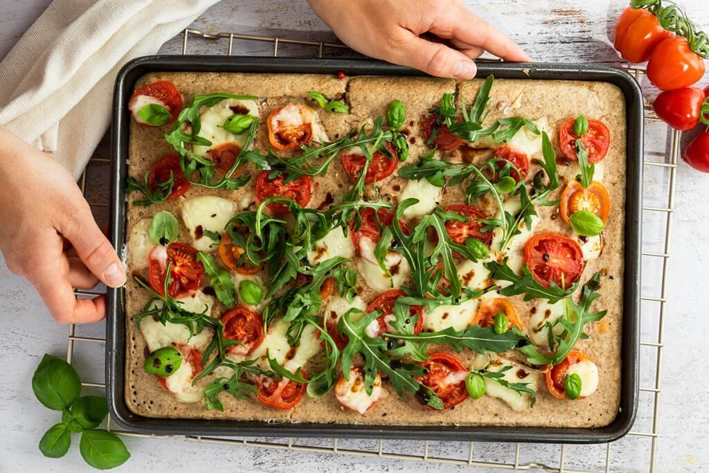 Ein Blech Pfannkuchen mit Tomaten, Mozzarella und Rucola.