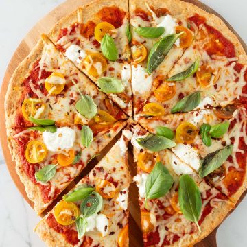 Eine Hand nimmt ein St&uuml;ck von einer gro&szlig;en Pizza mit High Protein Pizzateig weg.
