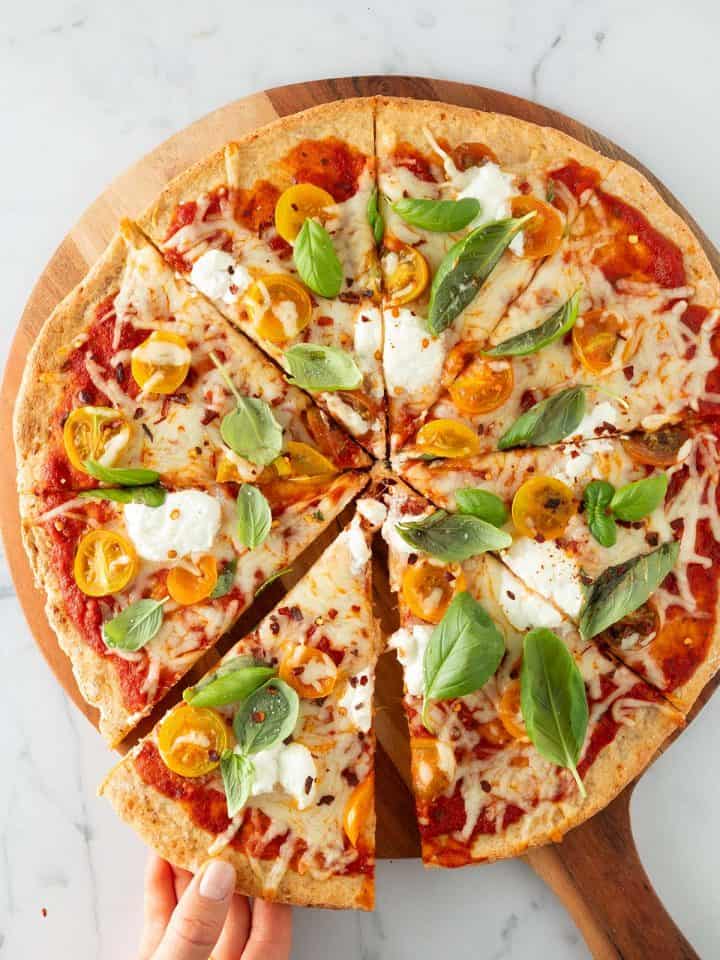 Eine Hand nimmt ein St&uuml;ck von einer gro&szlig;en Pizza mit High Protein Pizzateig weg.