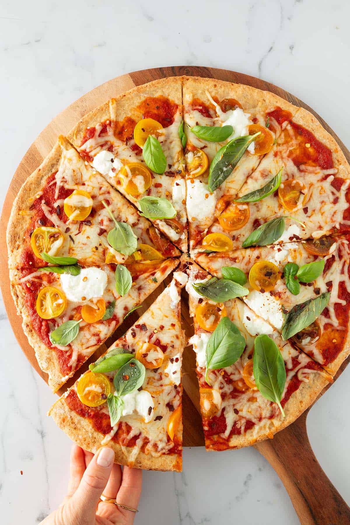 Eine Hand nimmt ein St&uuml;ck von einer gro&szlig;en Pizza mit High Protein Pizzateig weg.