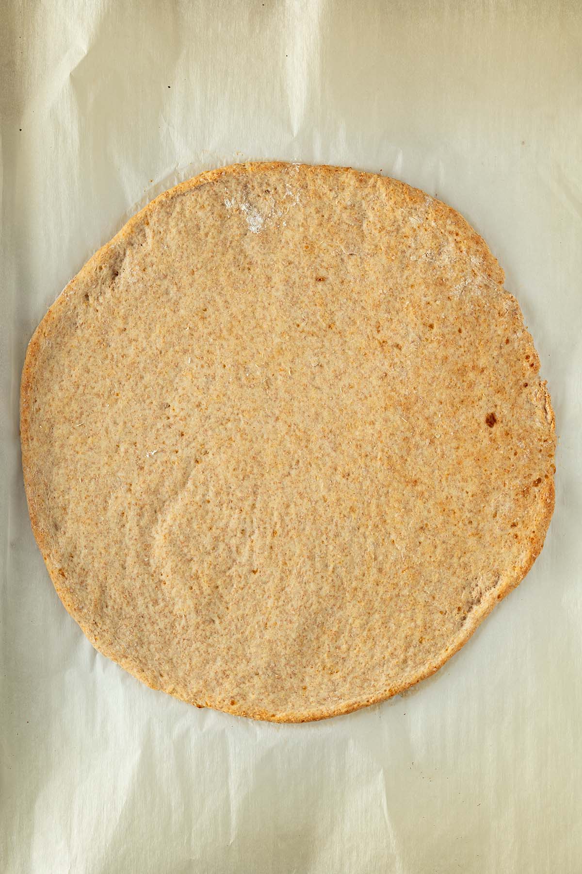Vorgebackener goldbrauner Protein Pizzateig auf Backpapier.