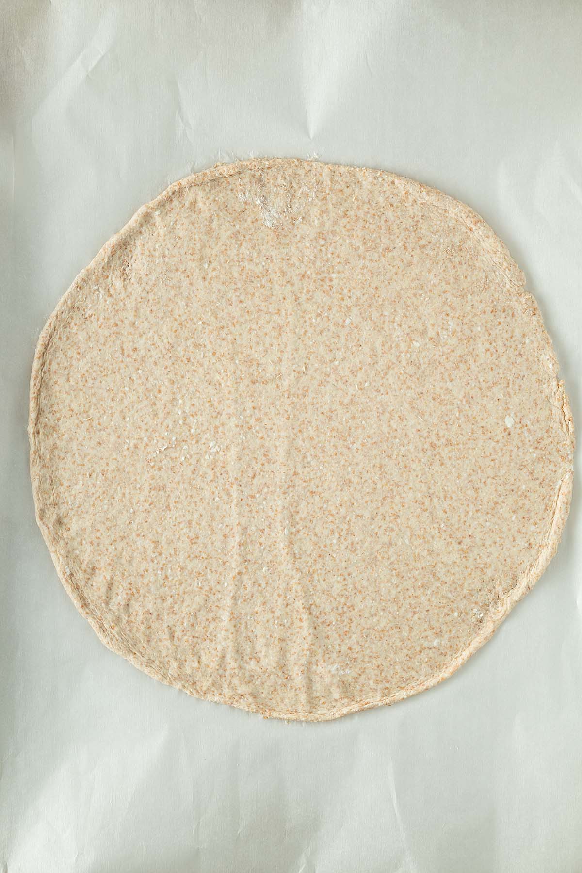 Ausgerollter Protein Pizzateig auf einem St&uuml;ck Backpapier.