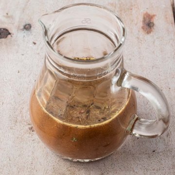 Kleine Glaskaraffe mit einem Balsamico-Honig-Senf-Dressing auf einem hellen Holzuntergrund.