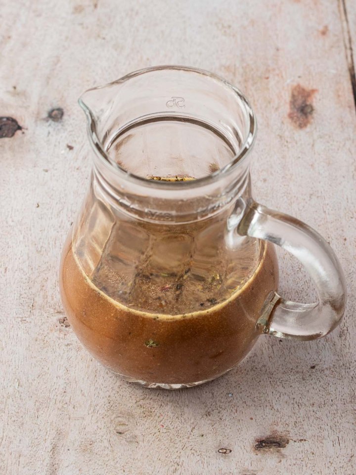 Kleine Glaskaraffe mit einem Balsamico-Honig-Senf-Dressing auf einem hellen Holzuntergrund.