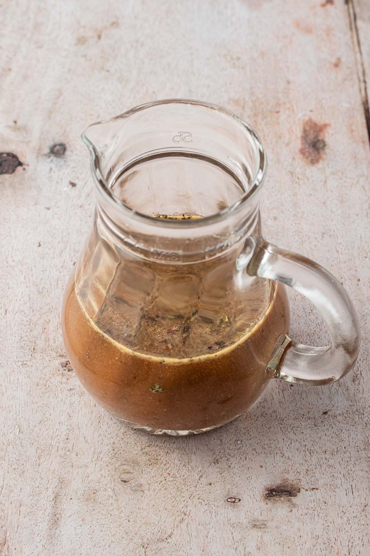 Kleine Glaskaraffe mit einem Balsamico-Honig-Senf-Dressing auf einem hellen Holzuntergrund.