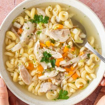 Eine Sch&uuml;ssel H&uuml;hnersuppe mit H&auml;hnchenfleisch, Gem&uuml;se und Suppennudeln in einem tiefen Teller.