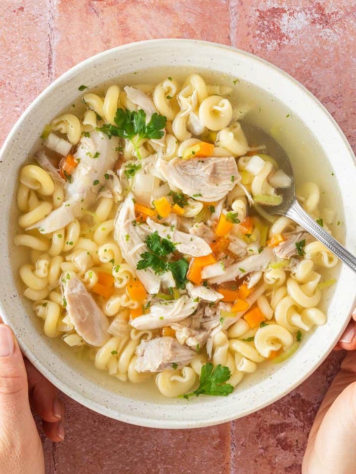 Eine Schüssel Hühnersuppe mit Hähnchenfleisch, Gemüse und Suppennudeln in einem tiefen Teller.