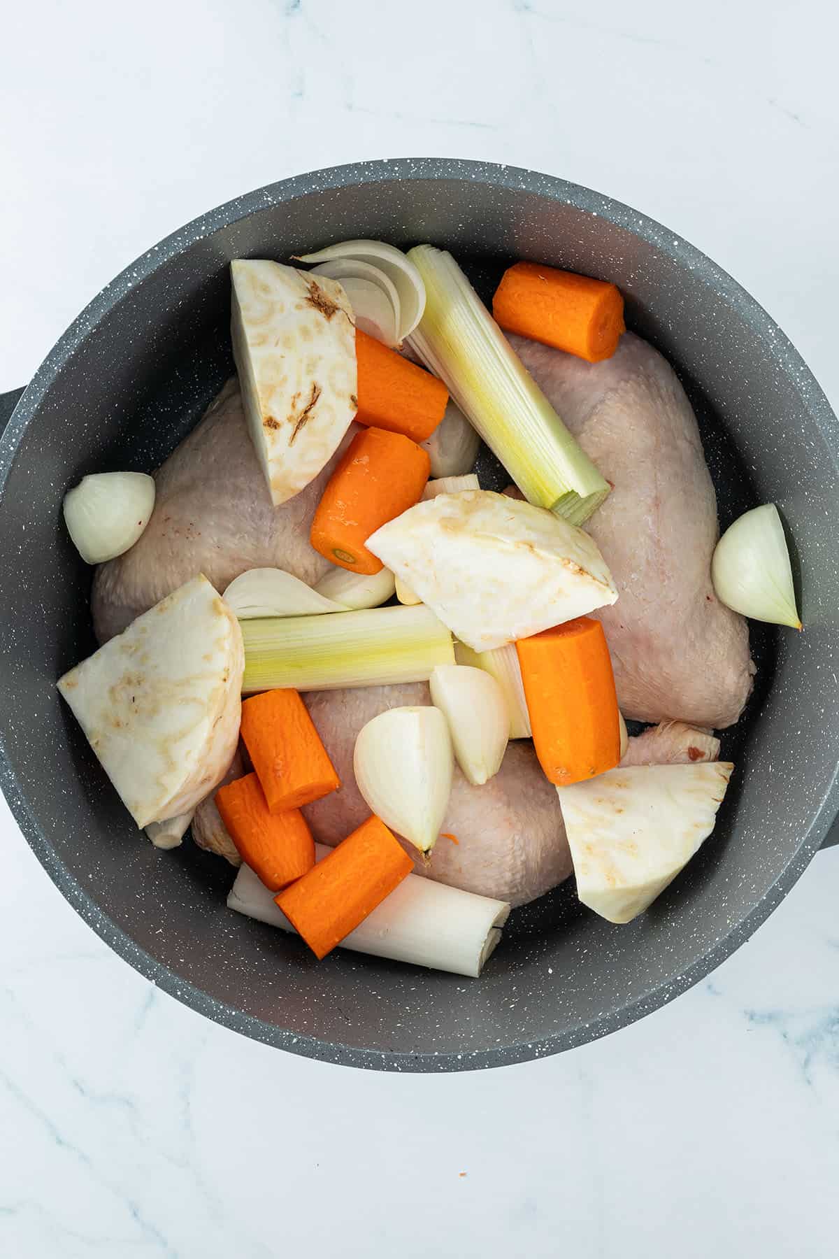 H&auml;hnchenschenkel und grob zerkleinertes Suppengem&uuml;se in einem Topf.