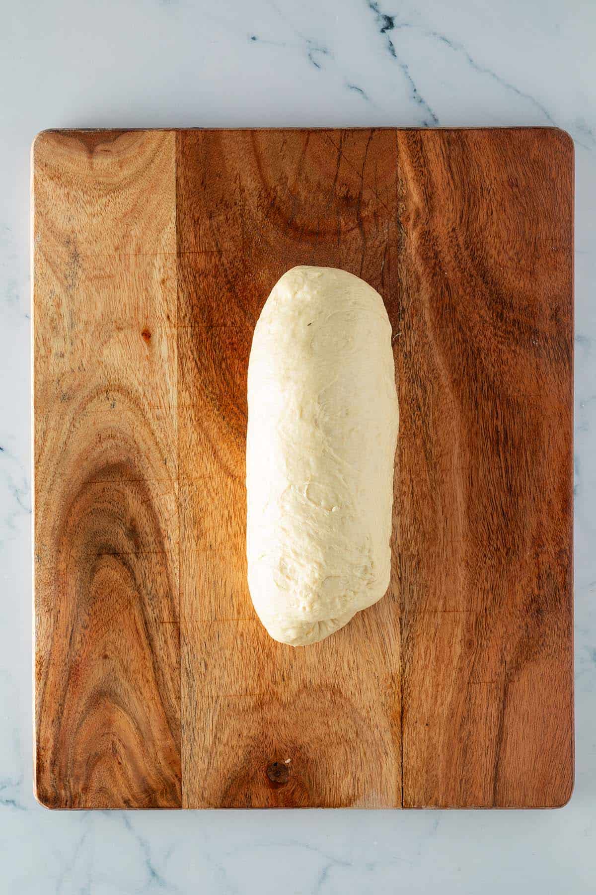 Geformter Toast-Brotteig als l&auml;nglicher Laib auf einem Holzbrett.