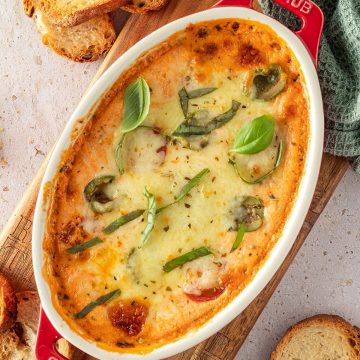 Mit K&auml;se &uuml;berbackener Pizza Dip, serviert in einer kleinen, ovalen Auflaufform mit knusprigen Brotchips und frischem Basilikum.