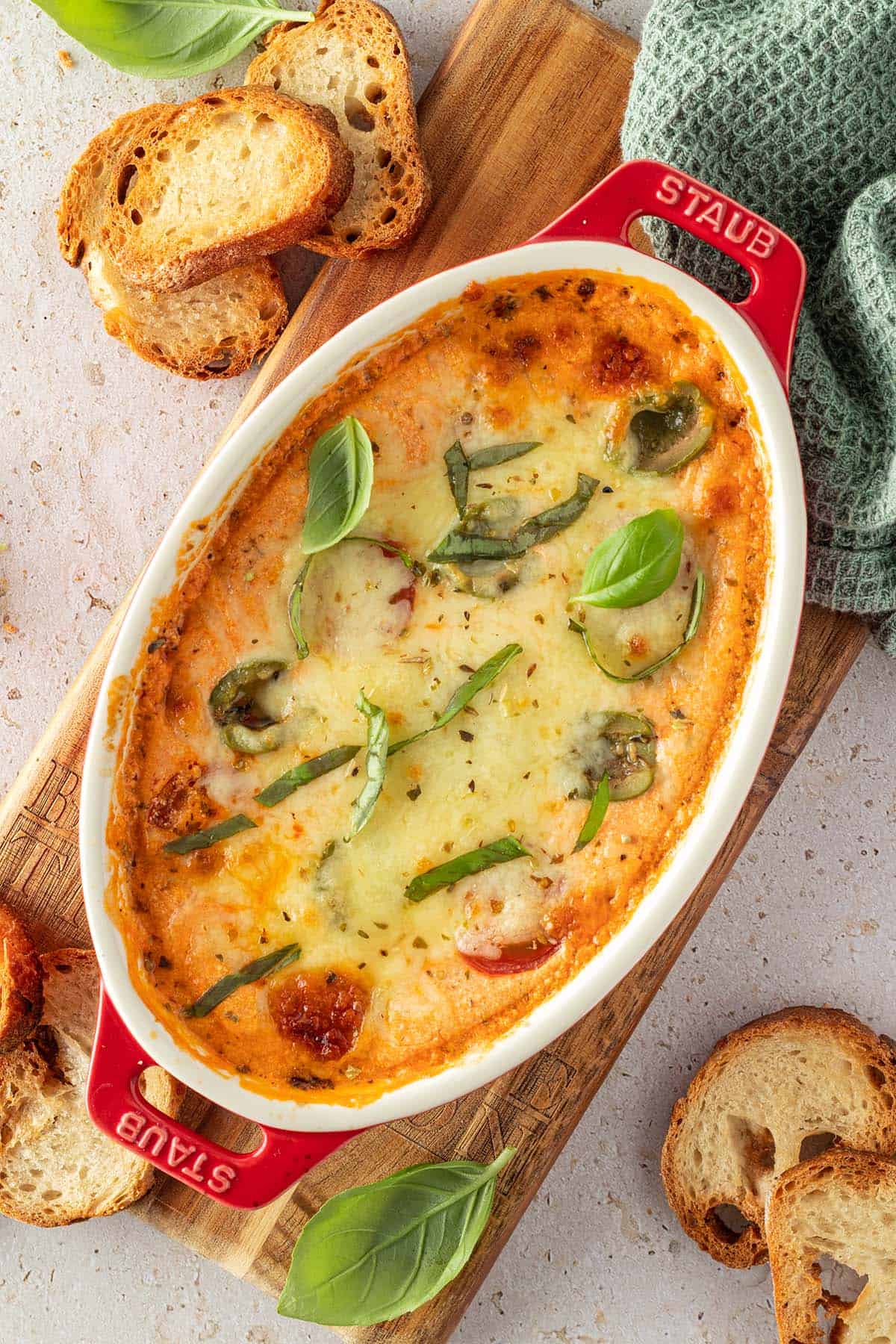 Mit K&auml;se &uuml;berbackener Pizza Dip, serviert in einer kleinen, ovalen Auflaufform mit knusprigen Brotchips und frischem Basilikum.