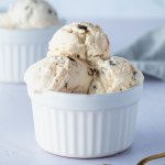 Mehrere Cottage-Cheese-Eis-Kugeln mit Schokost&uuml;ckchen in einer wei&szlig;en Sch&uuml;ssel, im Hintergrund eine zweite Sch&uuml;ssel mit Eiskugeln.