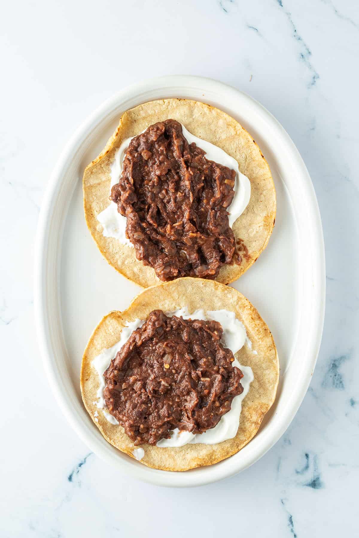 Zwei knusprig angebratene Tortillas mit Schmand und Refried Beans.