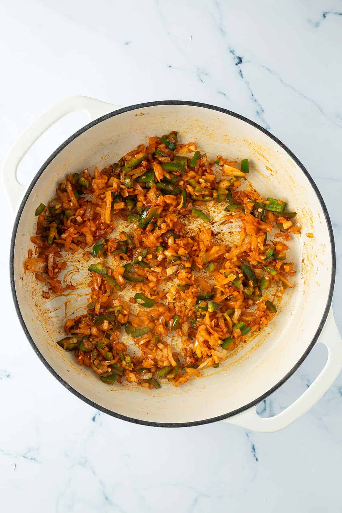 Zwiebeln, Knoblauch und Jalape&ntilde;o werden mit den Gew&uuml;rzen in der Pfanne angebraten.