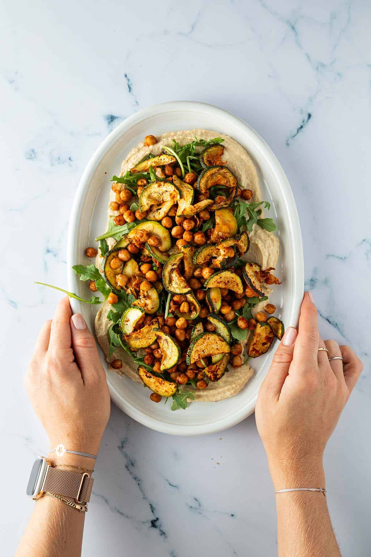 Platte mit Hummus-Dip, ger&ouml;steten Kichererbsen, Zucchini und Rucola.