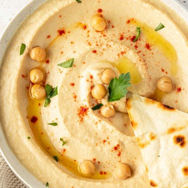 Eine Sch&uuml;ssel mit cremigen Hummus dekoriert mit ganzen Kichererbsen und frischen Kr&auml;utern.