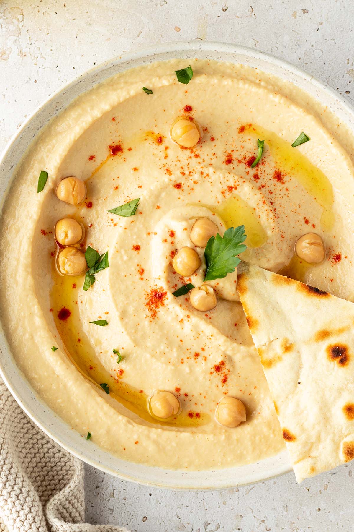 Eine Sch&uuml;ssel mit cremigen Hummus dekoriert mit ganzen Kichererbsen und frischen Kr&auml;utern.