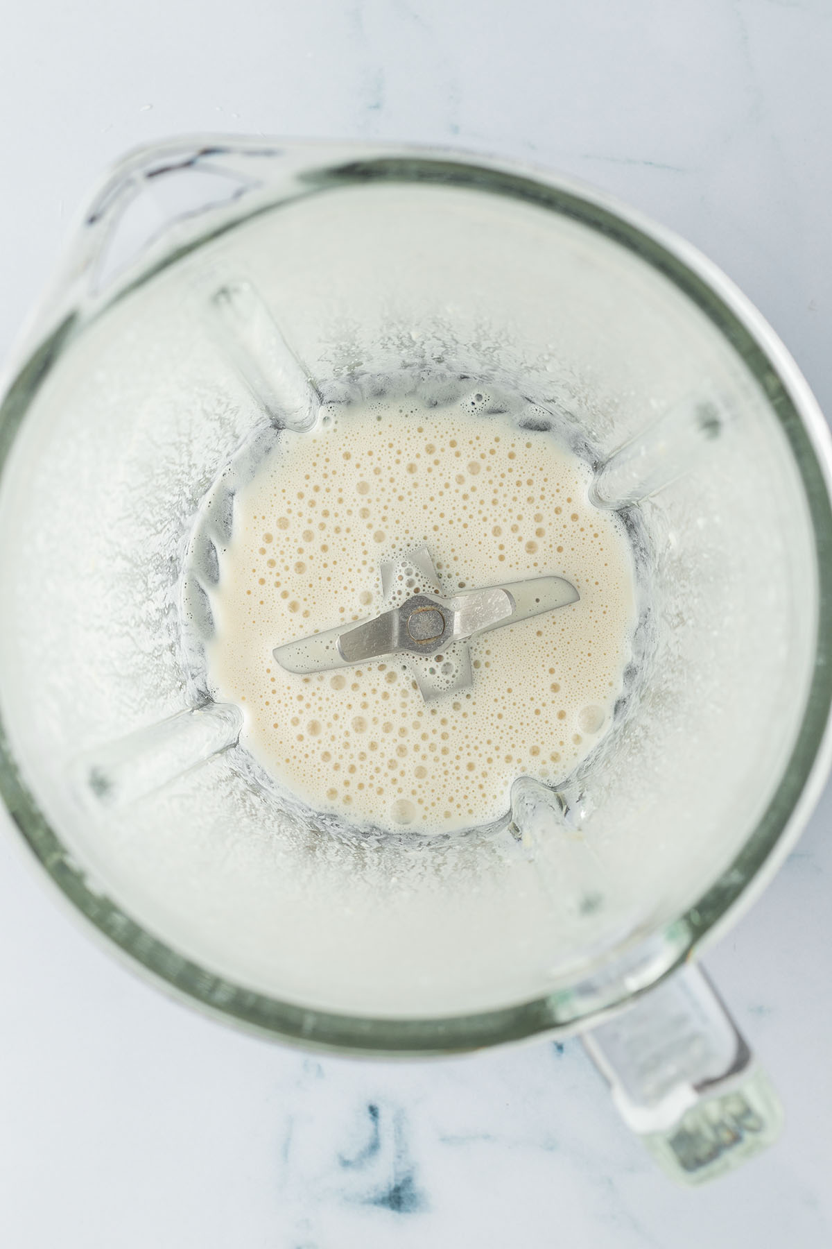 Vogelperspektive auf einen Standmixer mit einer cremig-wei&szlig;en, aber w&auml;ssrigen Fl&uuml;ssigkeit.