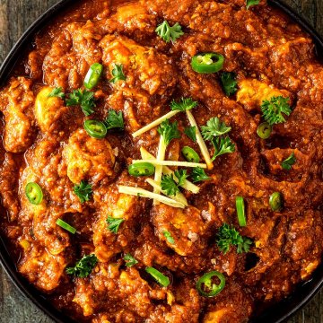 Foto von einer gro&szlig;en Sch&uuml;ssel mit einem indischen H&auml;hnchen Tikka Masala auf einem dunklen Holzuntergrund.