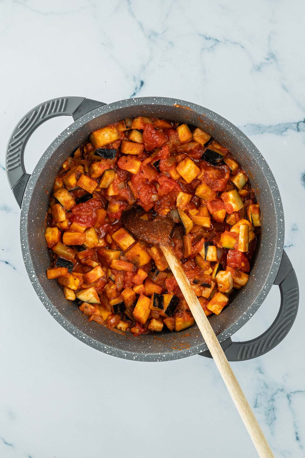 Vogelperspektive auf einen Topf mit kleingew&uuml;rfelten Auberginen in einer Tomatensauce.