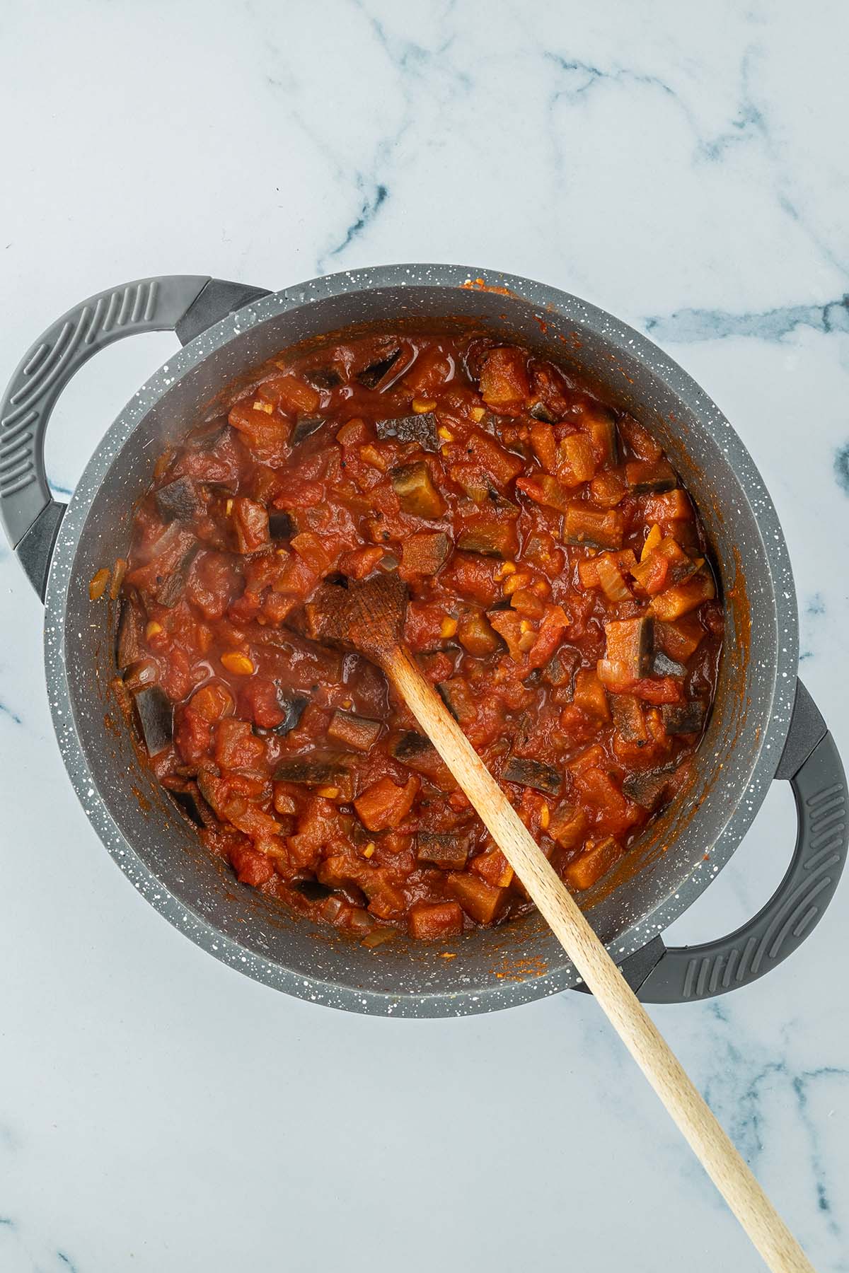 Vogelperspektive auf die Curry-Tomatensauce vor dem P&uuml;rieren mit weich gekochten Auberginen St&uuml;ckchen.