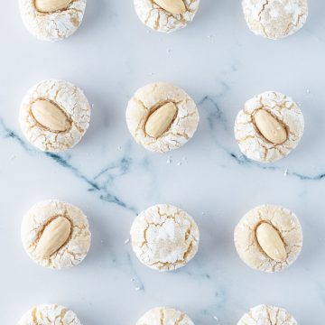12 weiche, italienische Mandelkekse mit und ohne Mandelkerne auf einem hellen Marmoruntergrund.