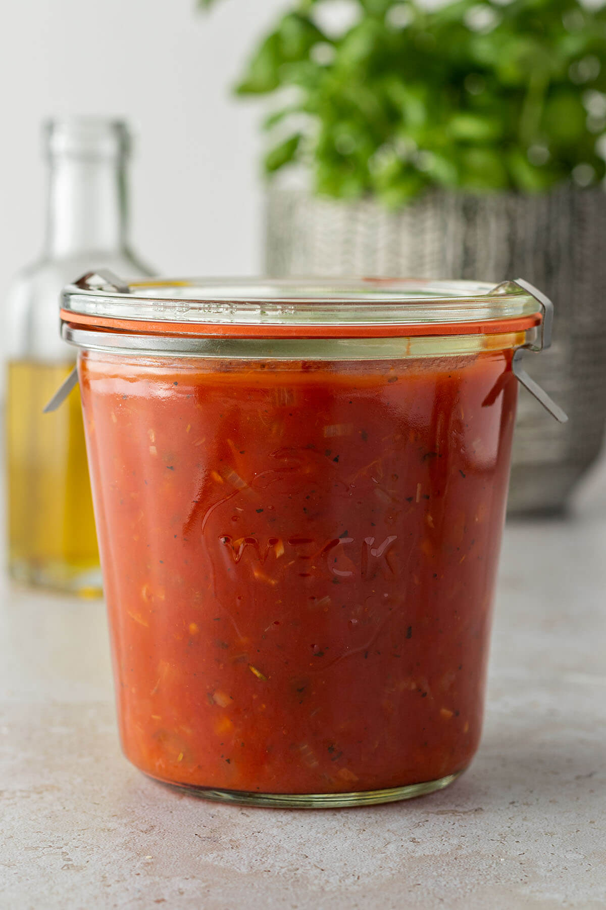 Ein Weckglas mit Tomatensauce, eine Flasche &Ouml;l und ein Topf Basilikum im Hintergrund.